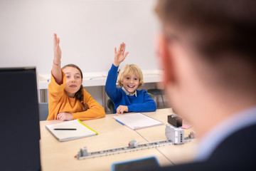 Pupils sitting at desk, raising their hands