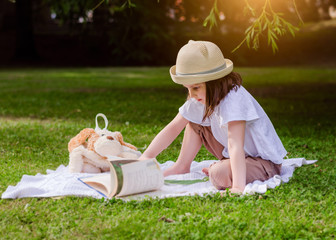 Preschooler girl in a straw hat in the park with book. Child in the park on a summer picnic.