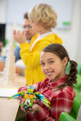 Girl holding buildable bird and smiling, boy and teacher building tower