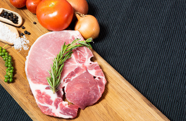 Top view raw pork chop meat on wood plate with vegetables, spices, salt and black pepper in dark black cloth table