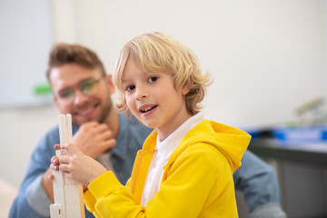 Boy fixing blocks, teacher looking at him, smiling