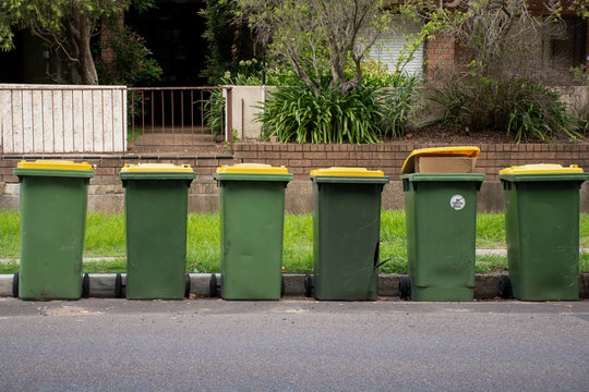 Australian garbage wheelie bins with yellow lids for recycling household waste lined up on the street kerbside for council rubbish collection.