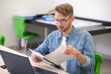 Male teacher sitting at laptop, checking notes