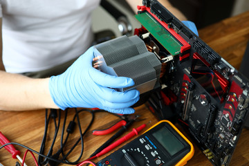 Close-up of persons hands in protective gloves working with computer detail. Voltmeter for measuring voltage laying on wooden table. Diy and hobby concept