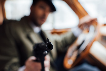 Selective focus of mafioso aiming gun while driving retro car
