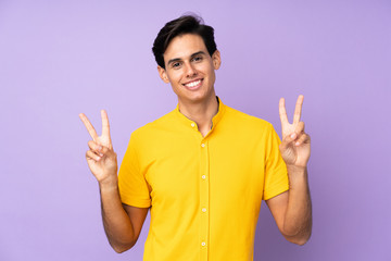 Man over isolated purple background showing victory sign with both hands