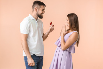 Young man proposing to his beloved on color background