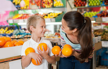 Fototapeta premium Portrait of happy woman and her little son choosing oranges at shop