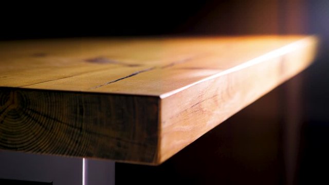Close-up of edge of wooden table on dark background. Stock footage. Beautiful smooth edge of brown wooden table lit by warm light on dark background