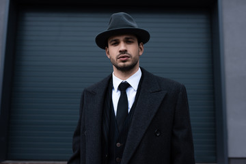 Front view of mafioso in black coat and felt hat on street - obrazy, fototapety, plakaty