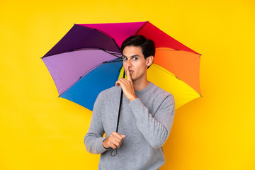 Man holding an umbrella over isolated yellow background doing silence gesture