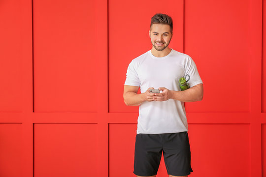 Sporty man with mobile phone on color background