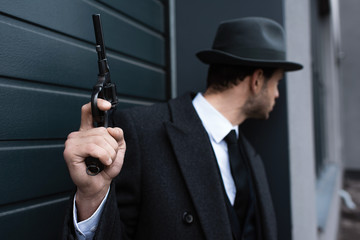 Selective focus of mafioso holding gun in corner on street
