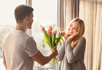 Romantic young man presenting flowers to his girlfriend at home