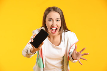 Screaming young woman with mobile phone on color background