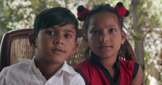 Indian brother sister seated together on a traditional seat or murrah as they look and pose for the camera smiling and inquisitively and whisper softly their names and speak with a toothy smile 