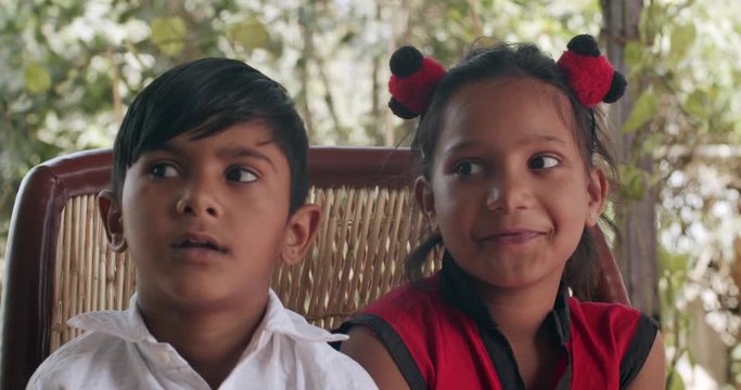 Indian brother sister seated together on a traditional seat or murrah as they look and pose for the camera smiling and inquisitively and whisper softly their names and speak with a toothy smile 