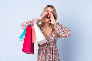 Teenager Russian girl with shopping bag isolated on blue background shouting and announcing something