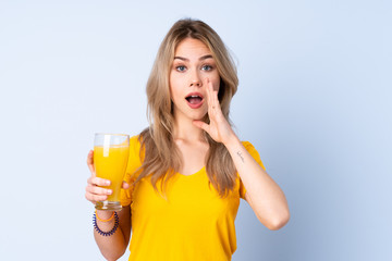 Teenager Russian girl holding an orange juice isolated on blue background shouting with mouth wide open