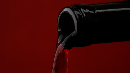 pouring red wine from bottle into wine glass, closeup. red background