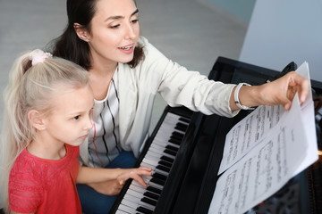 Private music teacher giving piano lessons to little girl