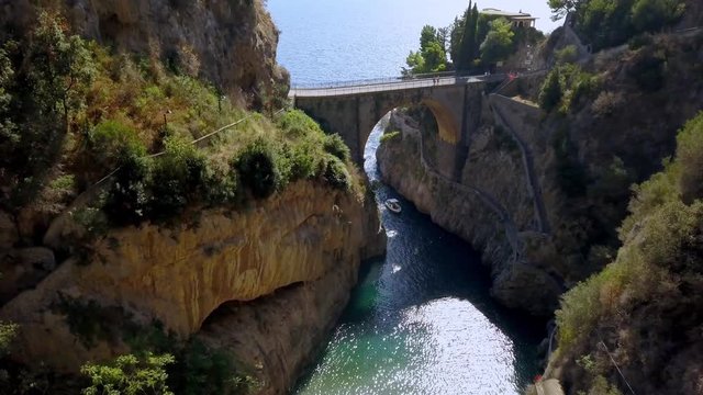 Fiordo di Furore arch bridge with a boat entering the passageway to village, Amalfi coast in Salerno Italy, Aerial approach down shot