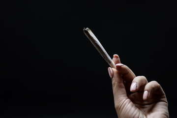 Woman hand holding cigarette. Smoking cannabis joint. Medical use. Black background.