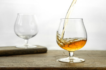 Cognac \ whiskey in cognac glass on wooden table, golden color spirits splashing on white background