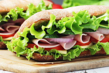 Two sandwiches with fresh vegetables, ham and cheese in ciabatta bread	