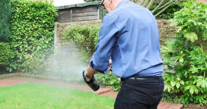 Senior man washing shoes in garden with a hose