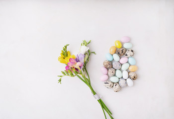 Chocolate Easter eggs glazed with pastel coloring and quail eggs over white background. Fresh colorful wildflowers. Happy Easter concept. Copy space. Top view