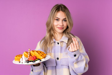 Teenager Russian girl holding waffles isolated on purple background making money gesture