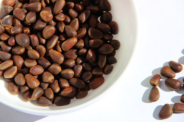 Unpeeled cedar pine nuts in white plate on white background
