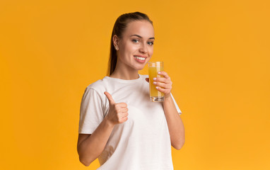 Happy woman holding glass with orange juice and gesturing thumb up