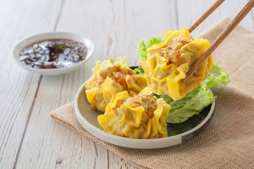 Chinese Steamed Dumpling, Shumai on white dish served with soy sauce and .lettuce leaves on brown cloth and wooden table. Delicious Dimsum pork.