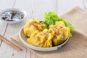 Chinese Steamed Dumpling, Shumai on white dish served with soy sauce and .lettuce leaves on brown cloth and wooden table. Delicious Dimsum pork.