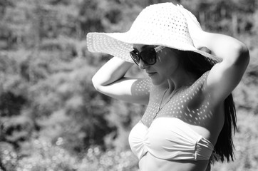 Girl in a hat and glasses in a swimsuit posing on the beach