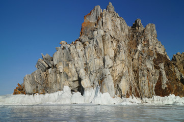 Fototapeta na wymiar a rock rises from a frozen lake against a blue sky