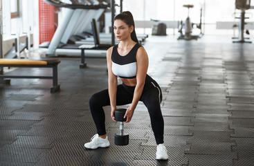 Young woman with dumbbell doing squats in gym
