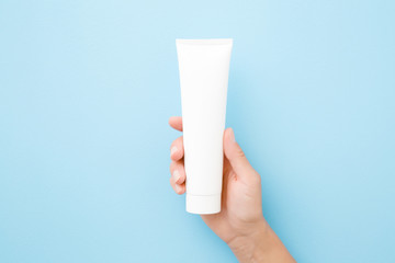 Young woman hand holding and showing white tube on light blue background. Pastel color. Care about clean and soft body skin. Daily beauty product. Closeup. Top down view.