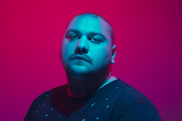 Portrait of a guy with colorful neon light on red studio background. Male model with calm and serious mood. Facial expression, cyberpunk, millenials lifestyle and look like. Future, technologies.