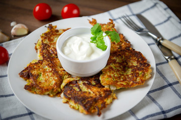 zucchini pancakes on a plate with sour cream and a sprig of coriander, cherry tomatoes , towel,...