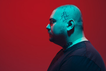 Portrait of a guy with colorful neon light on red studio background. Male model with calm and serious mood. Facial expression, cyberpunk, millenials lifestyle and look like. Future, technologies.