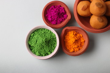 Popular Indian Sweet Besan Laddoo or gram flour sweet balls popular Holi snacks served in earthen bowl with variety of Traditional Holi colors. (Holi Food Concept)
