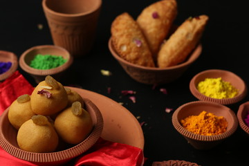 Popular Indian Sweet Besan Laddoo gram flour sweet balls and Gujia or Karanji arepopular Holi snacks served in earthen bowls.