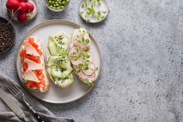 Sandwiches on toast with ingredients, vegetables, radishes, tomatoes, cucumbers and microgreens on gray. View from above.
