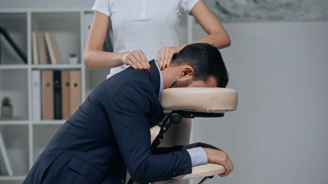 partial view of masseuse making neck massage to businessman in massage chair