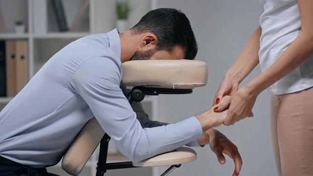 cropped view of masseuse making hands massage to businessman in massage chair