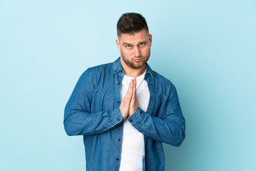 Russian handsome man isolated on blue background keeps palm together. Person asks for something