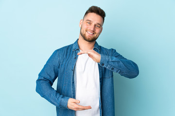 Russian handsome man isolated on blue background holding copyspace imaginary on the palm to insert...